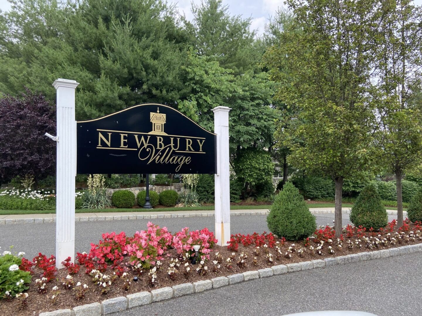 A sign that says newbury village with flowers in the foreground.