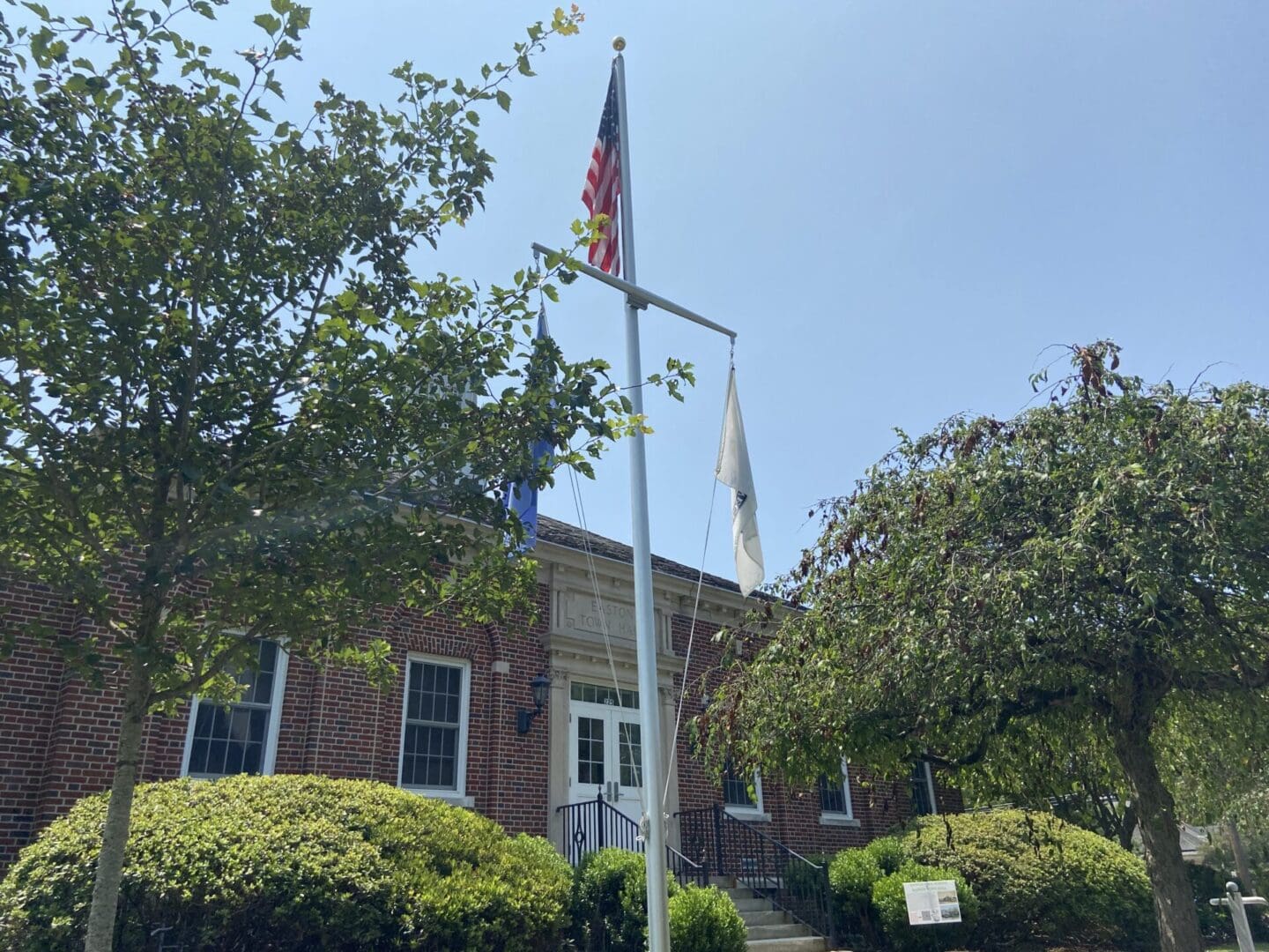 A flag pole in front of a building with trees.