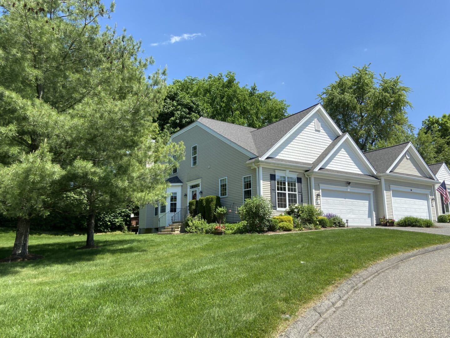 Tan house with green lawn and trees.