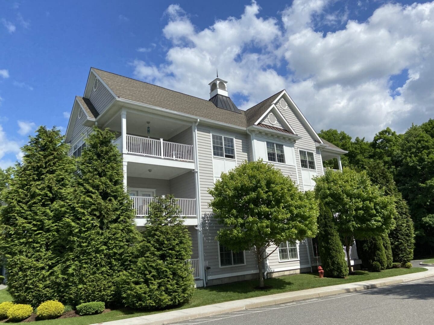 Gray multi-story house with green trees.