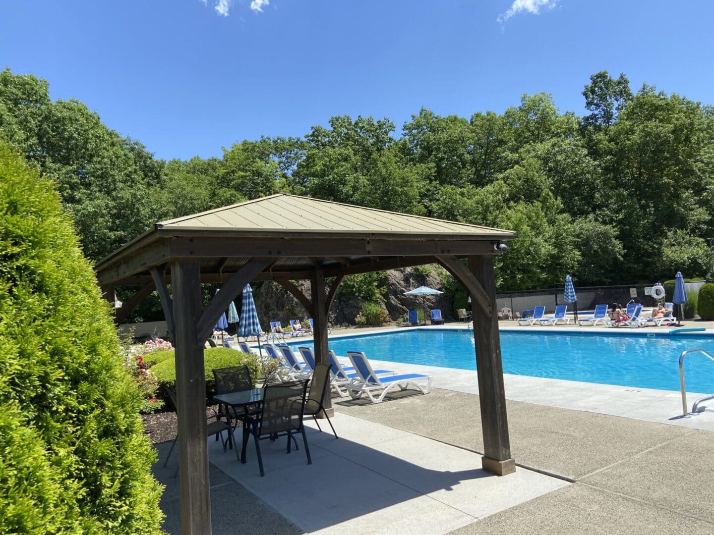 Poolside gazebo with chairs and trees.