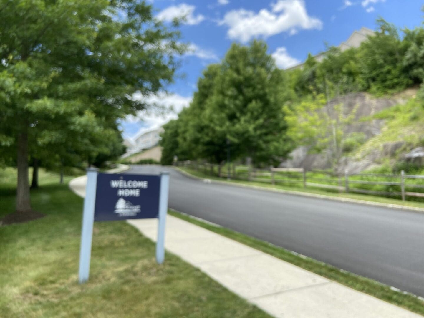 Welcome home sign with trees and road.