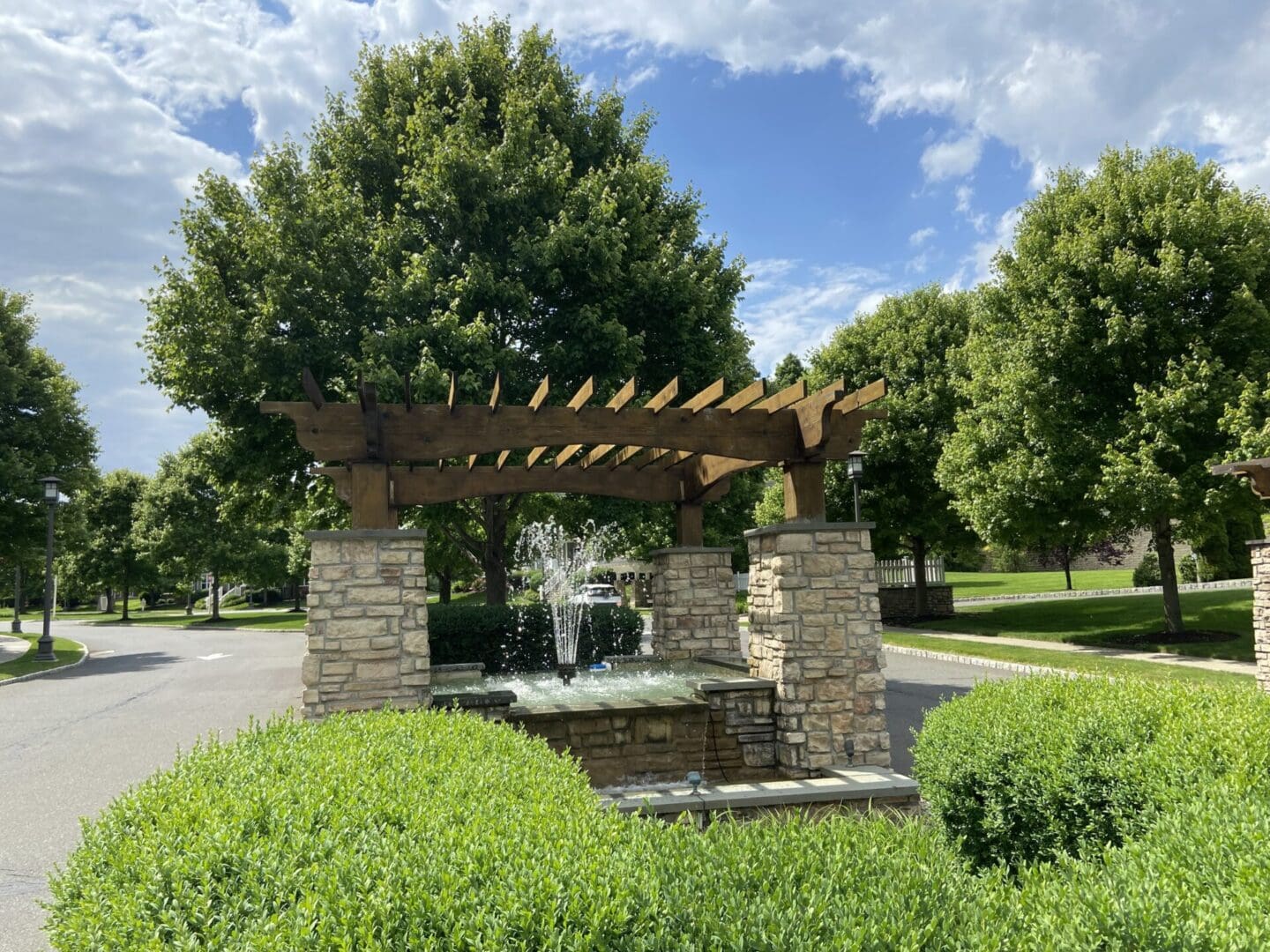 Stone fountain with wooden pergola and trees.