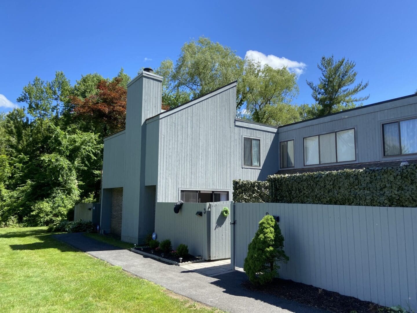 Gray siding house with green fence and trees.