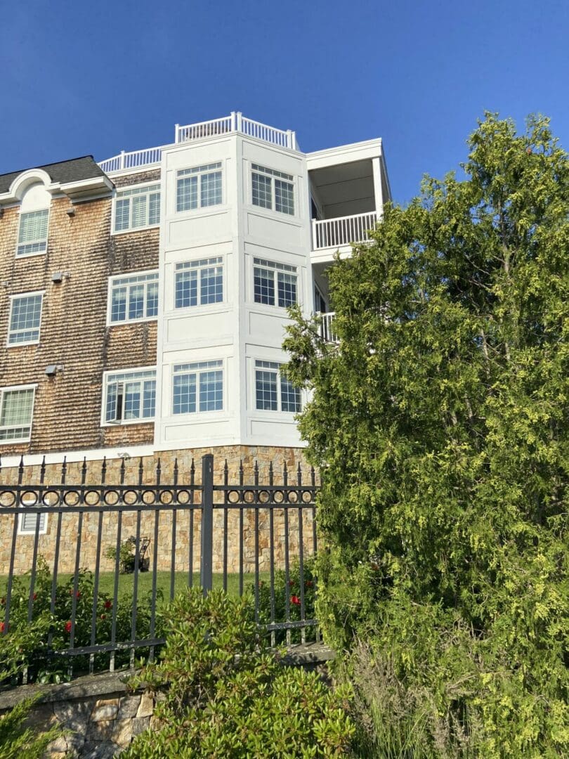 White building with black fence and green trees.