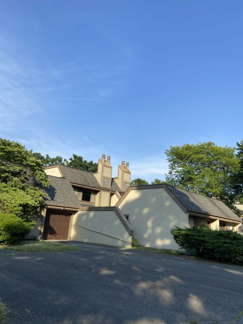 A tan house with a driveway and green trees.