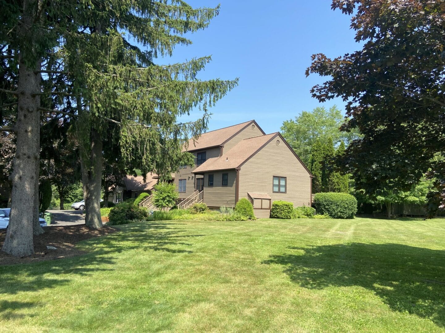 Tan house with green lawn and trees.