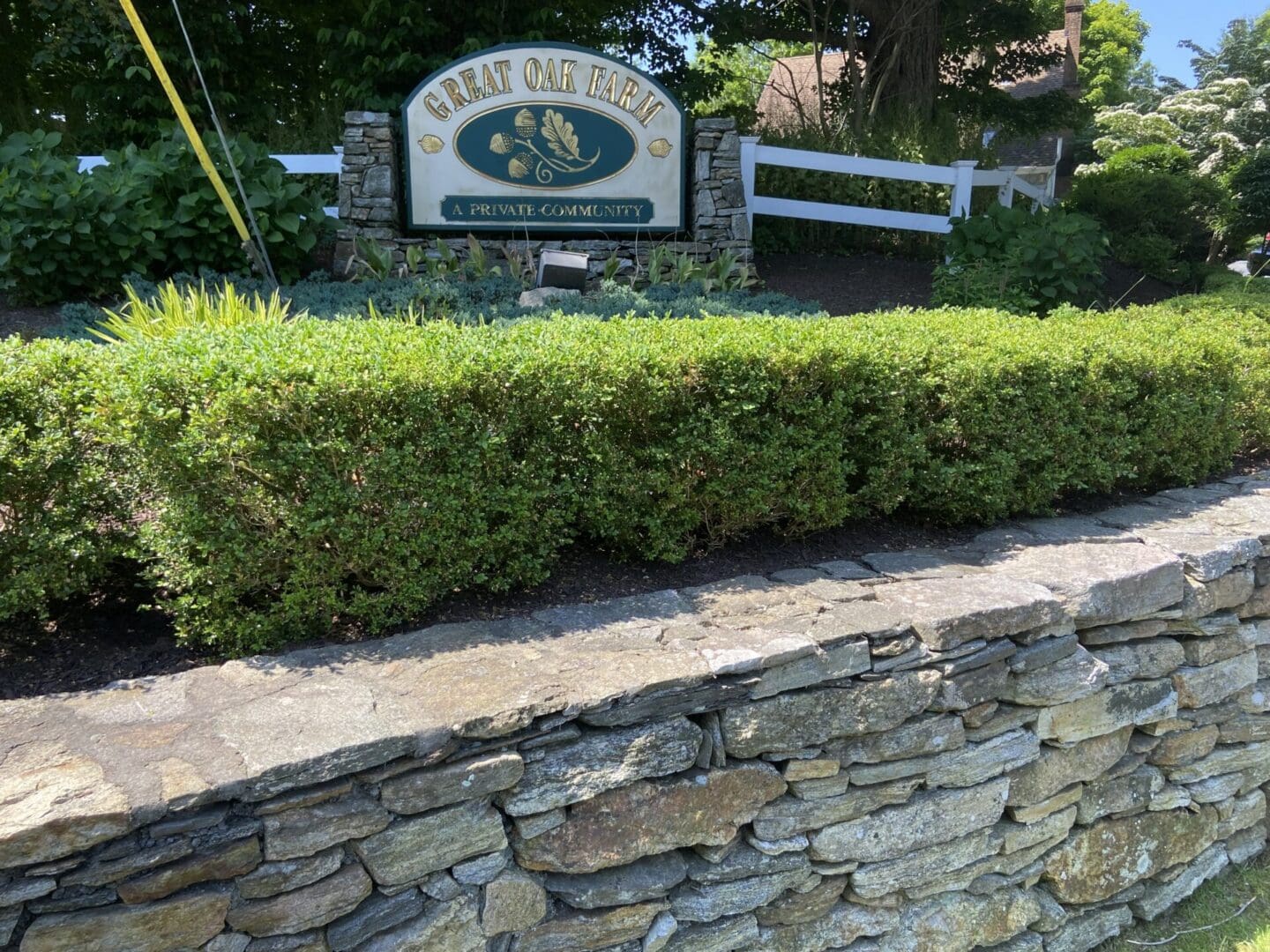 Stone wall with green hedge and sign.