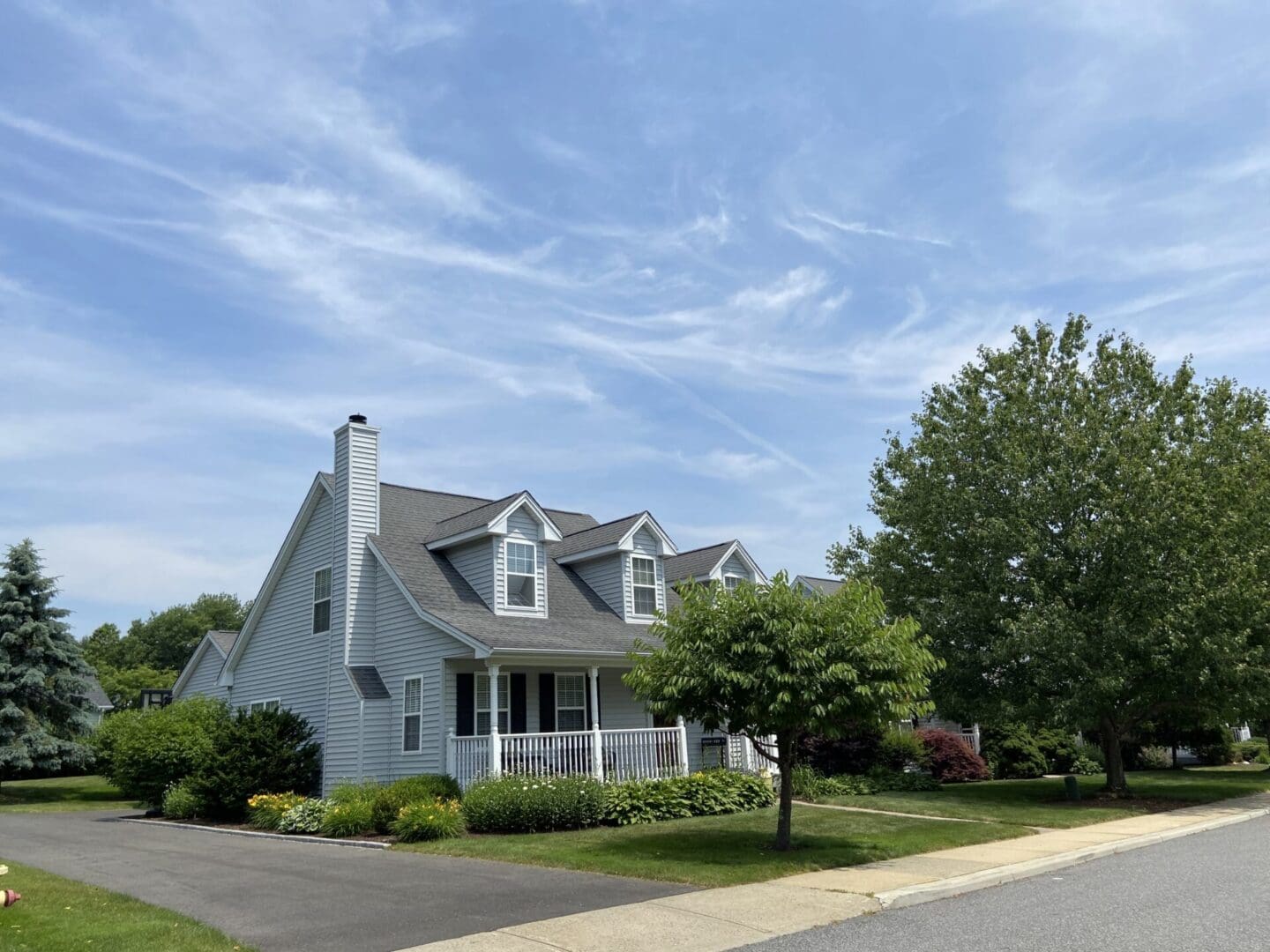 Gray suburban house with porch and trees.