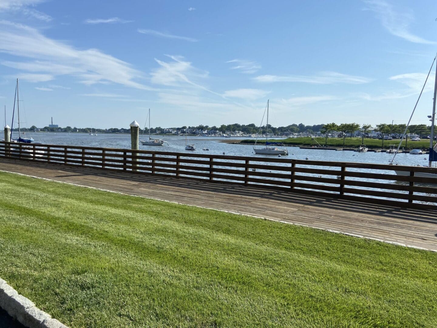 Harbor boardwalk with boats and grass.