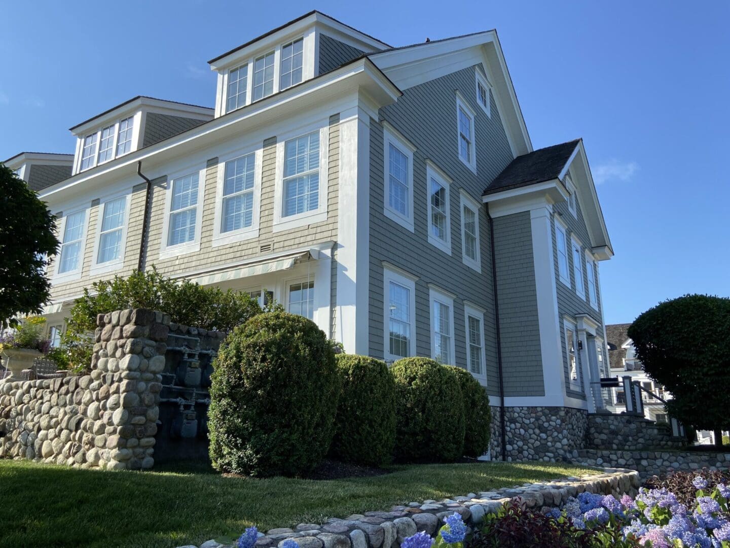 Gray house with stone wall and flowers.