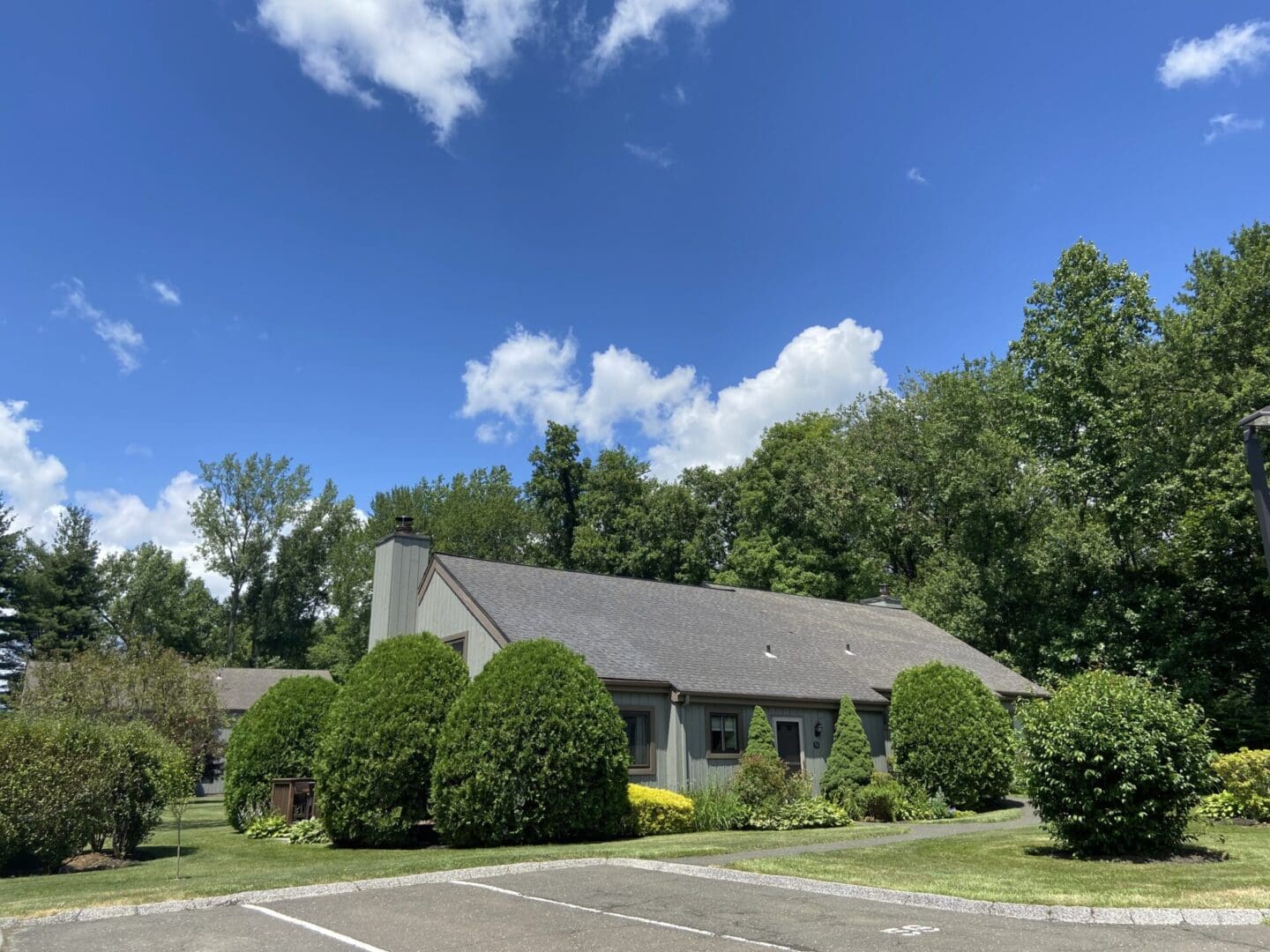 Gray house with green trees and blue sky.