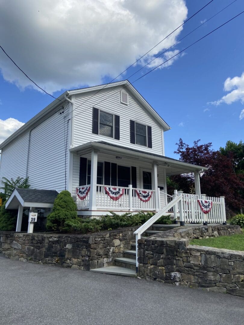 White house with porch and stone wall.