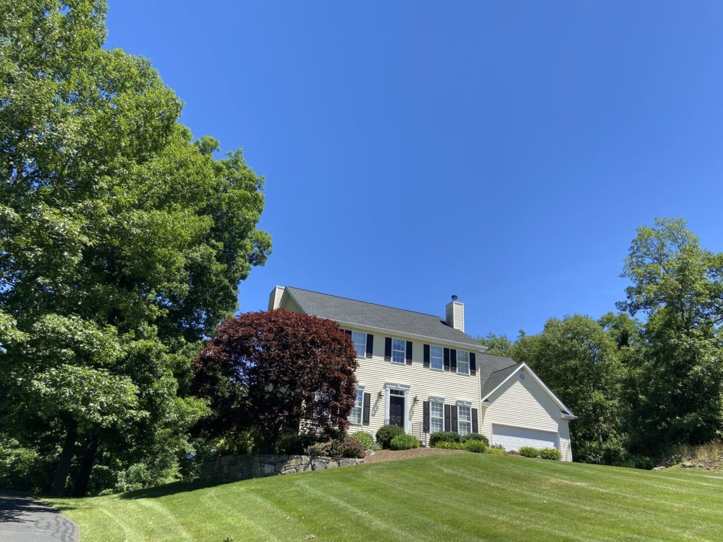 Yellow house with green lawn and trees.