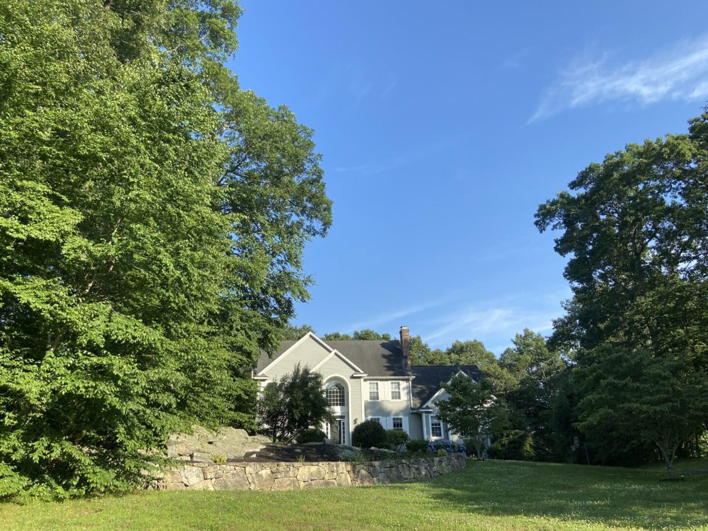 Green house with stone wall and trees.