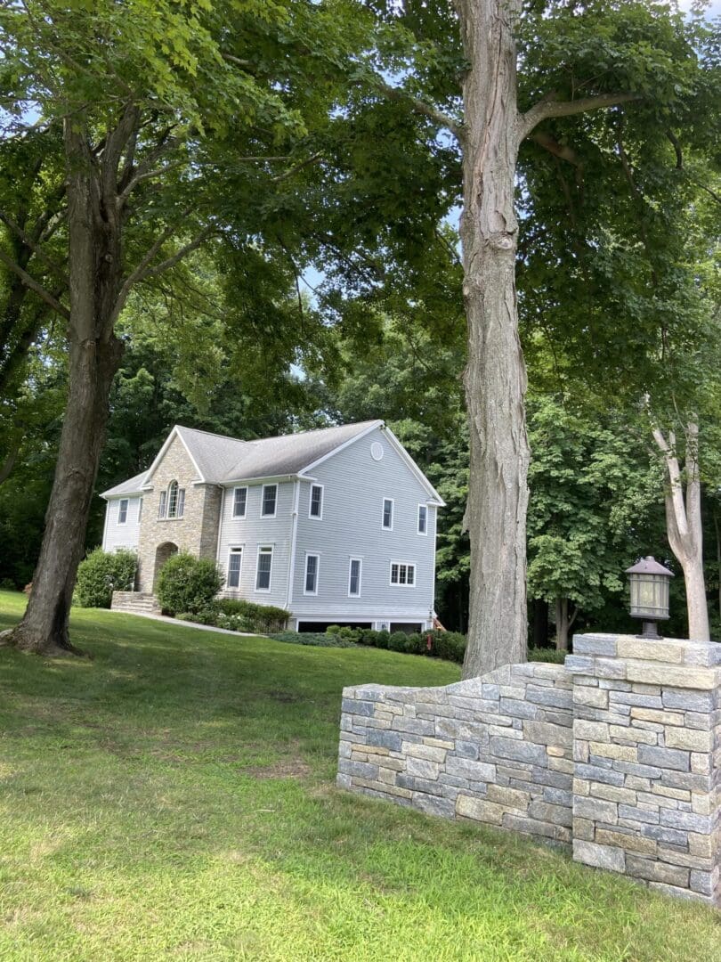 Grey house with stone wall and trees.