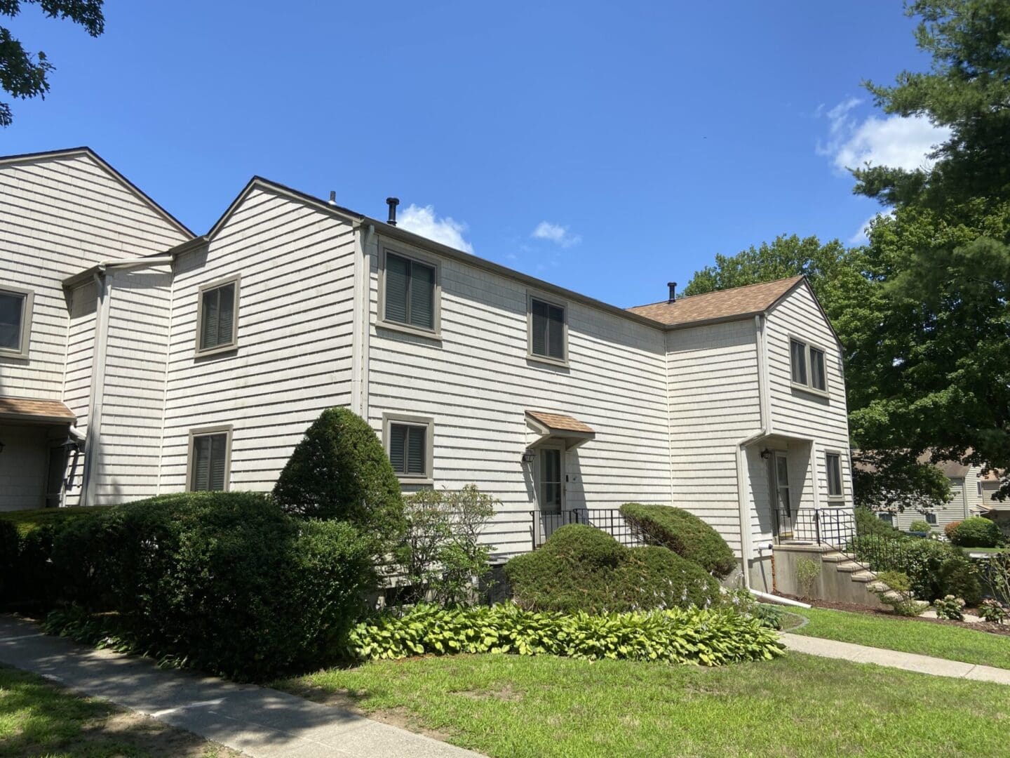 White siding townhouse with green bushes.