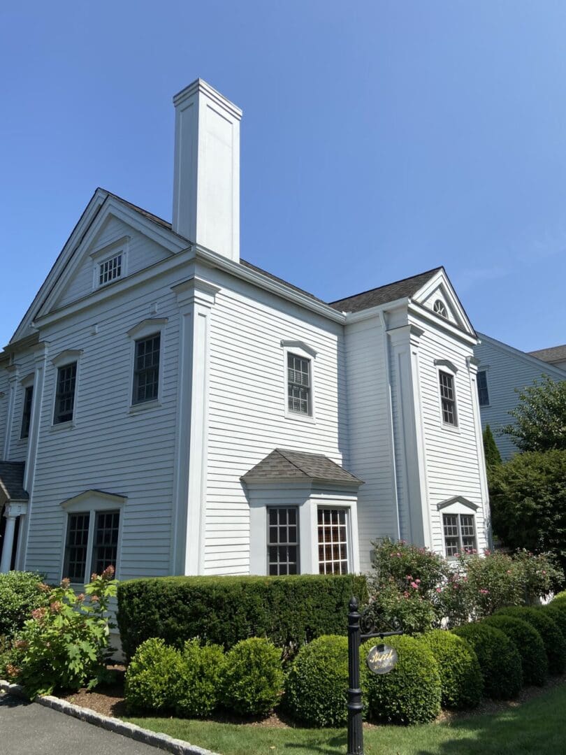 White colonial-style house with hedges.