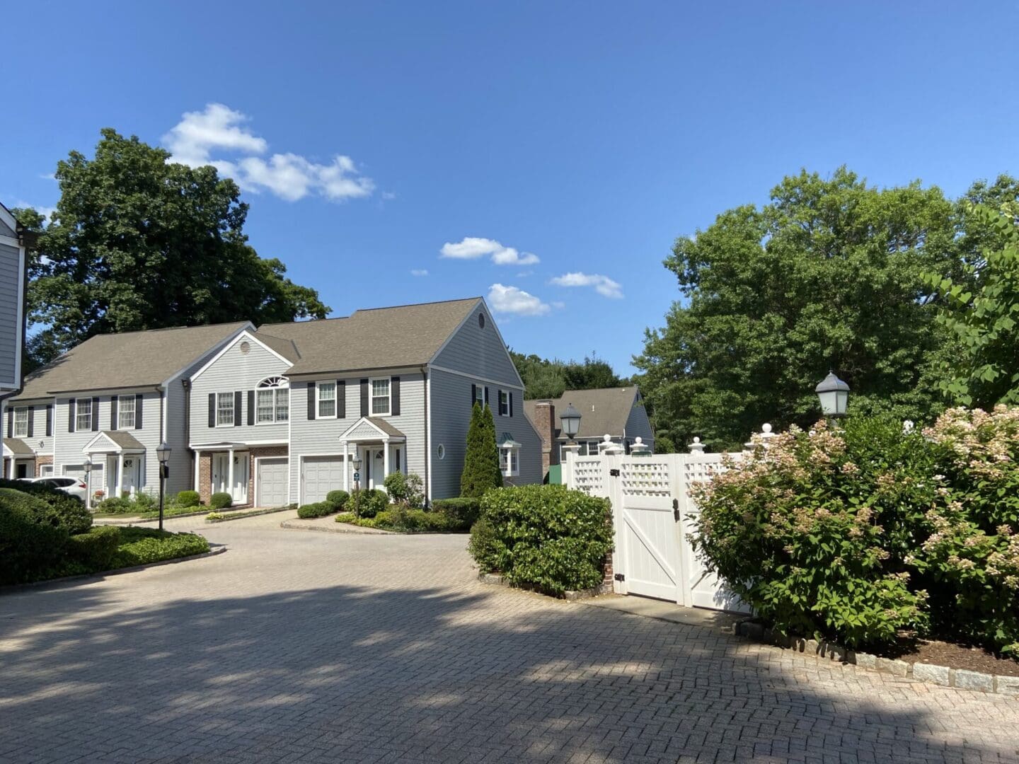 Gray townhouses, sunny driveway, white gate.