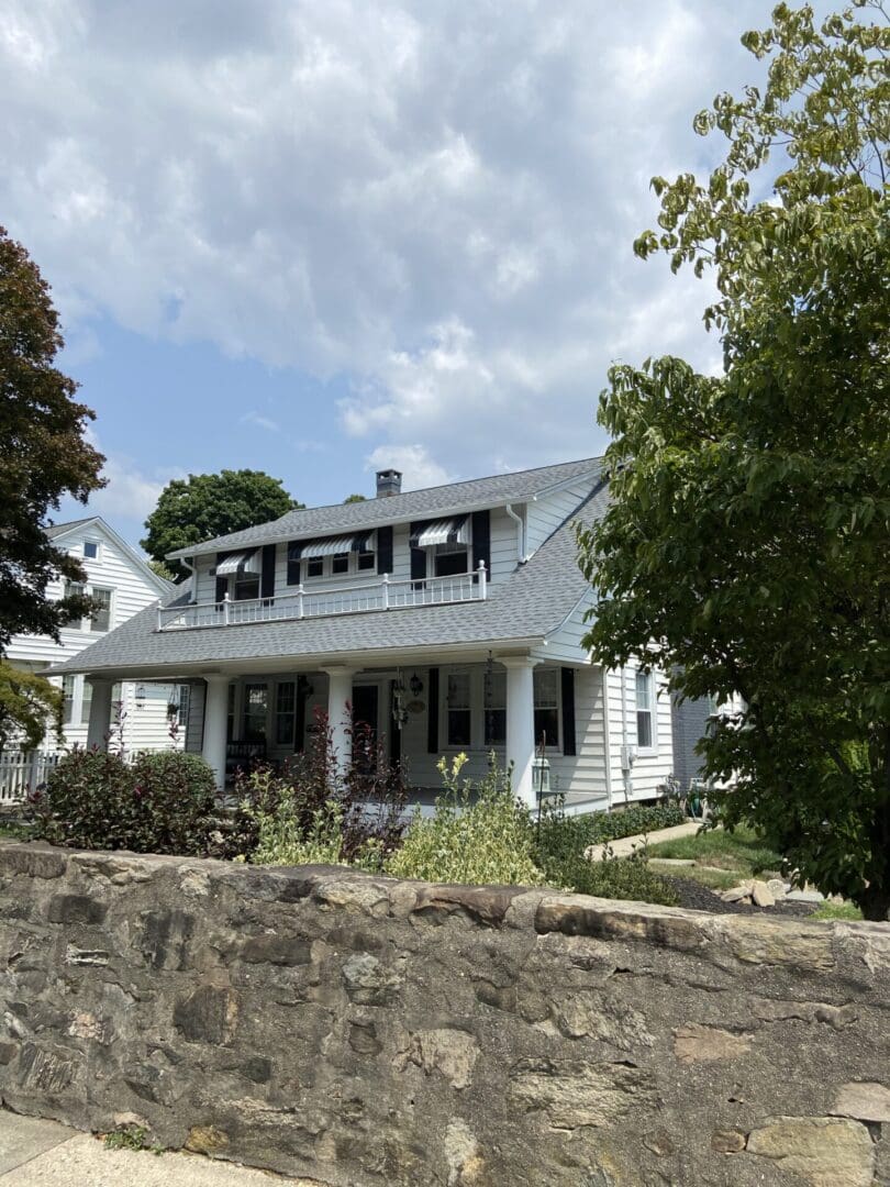 White house with black awnings and stone wall.