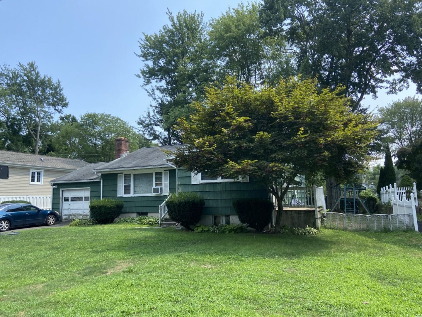 Green suburban home with trees and lawn.