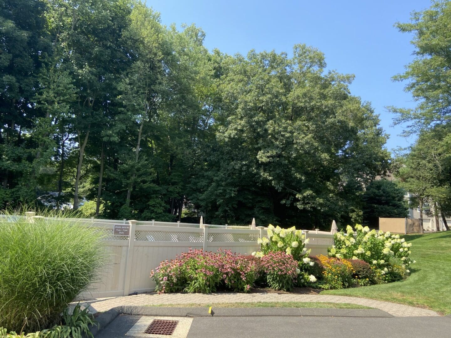 White fence with green trees and flowers.