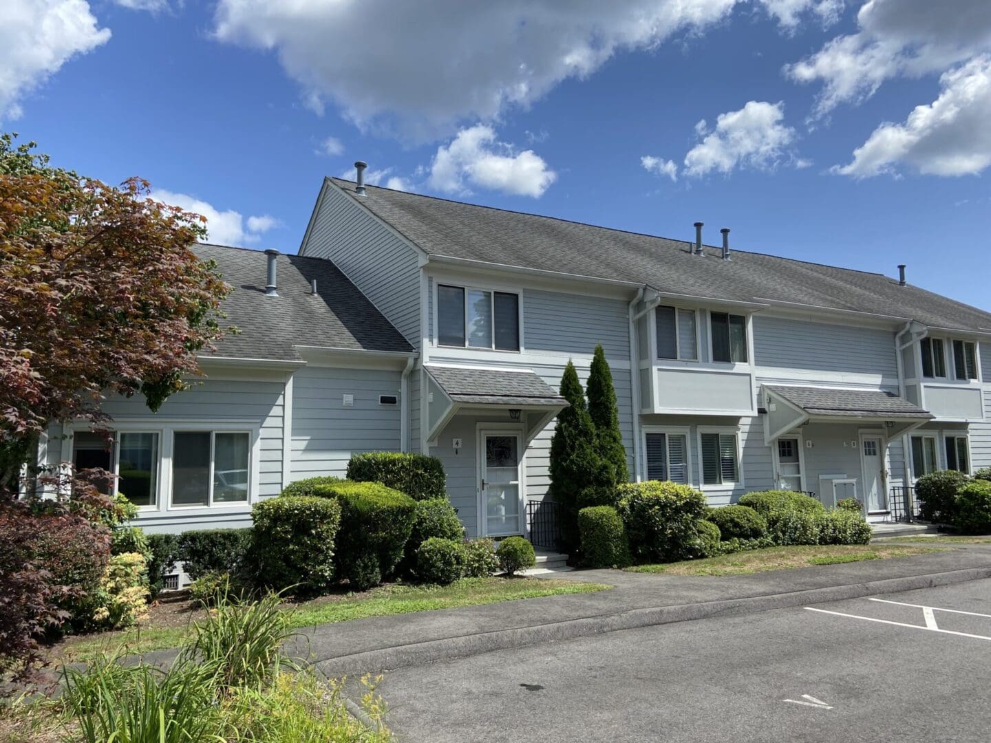 Gray townhouse with green shrubbery and a driveway.