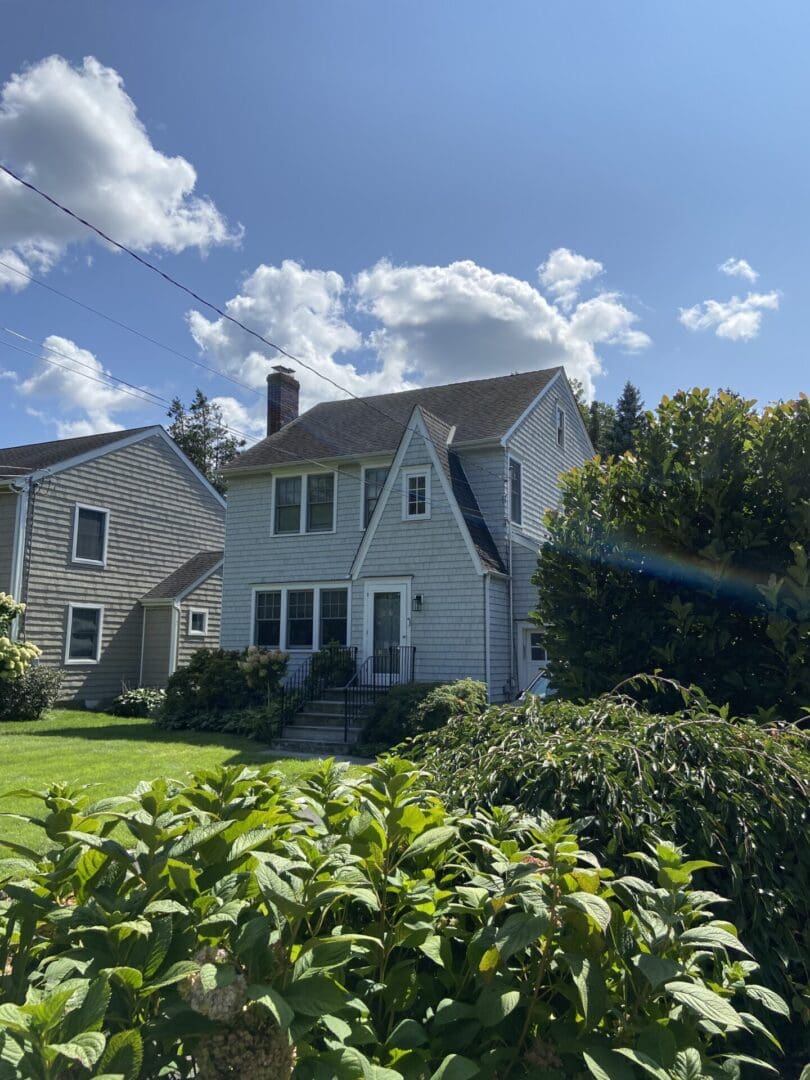 Gray house, sunny day, green bushes.