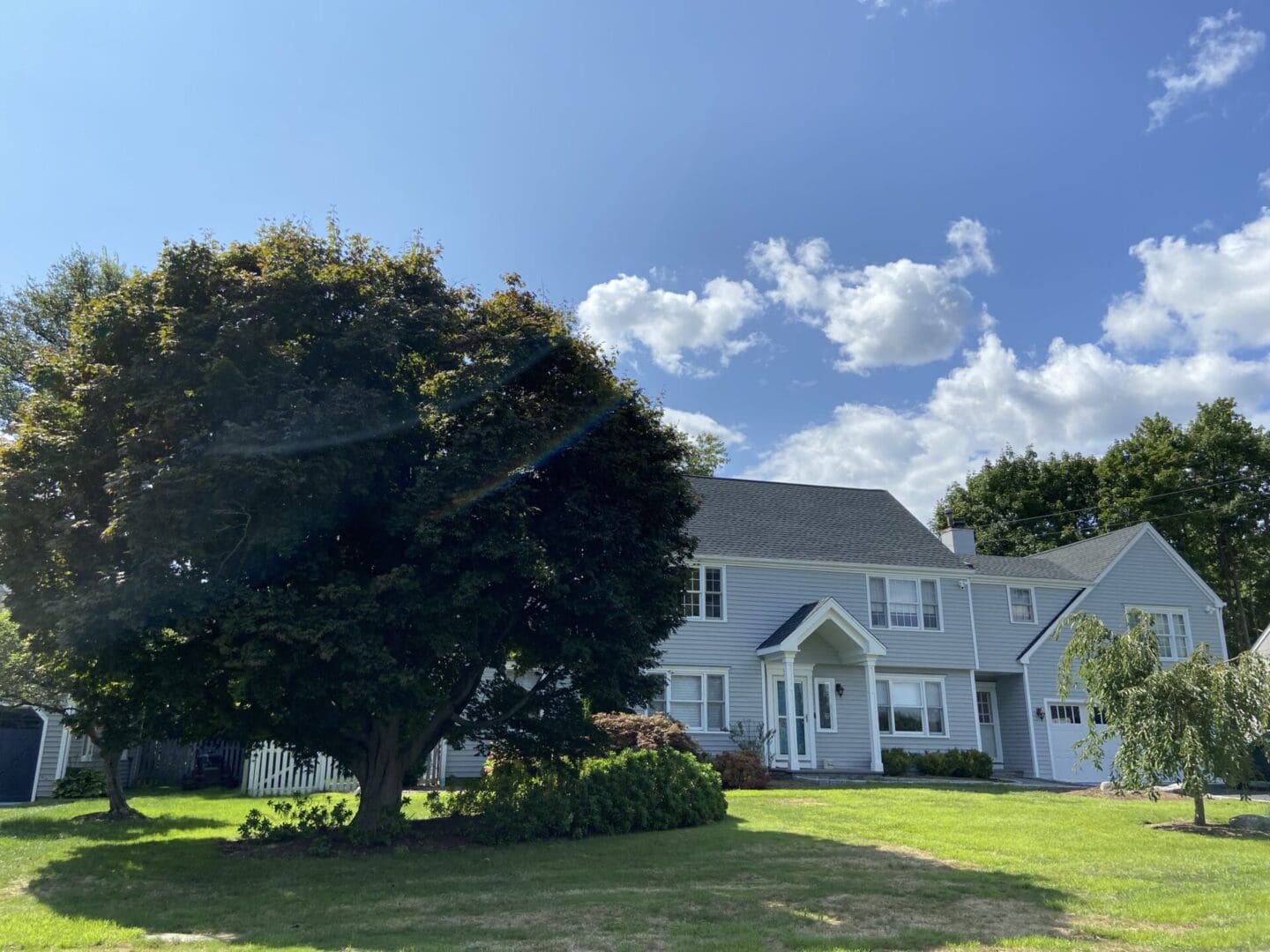 Gray house, large tree, sunny day.