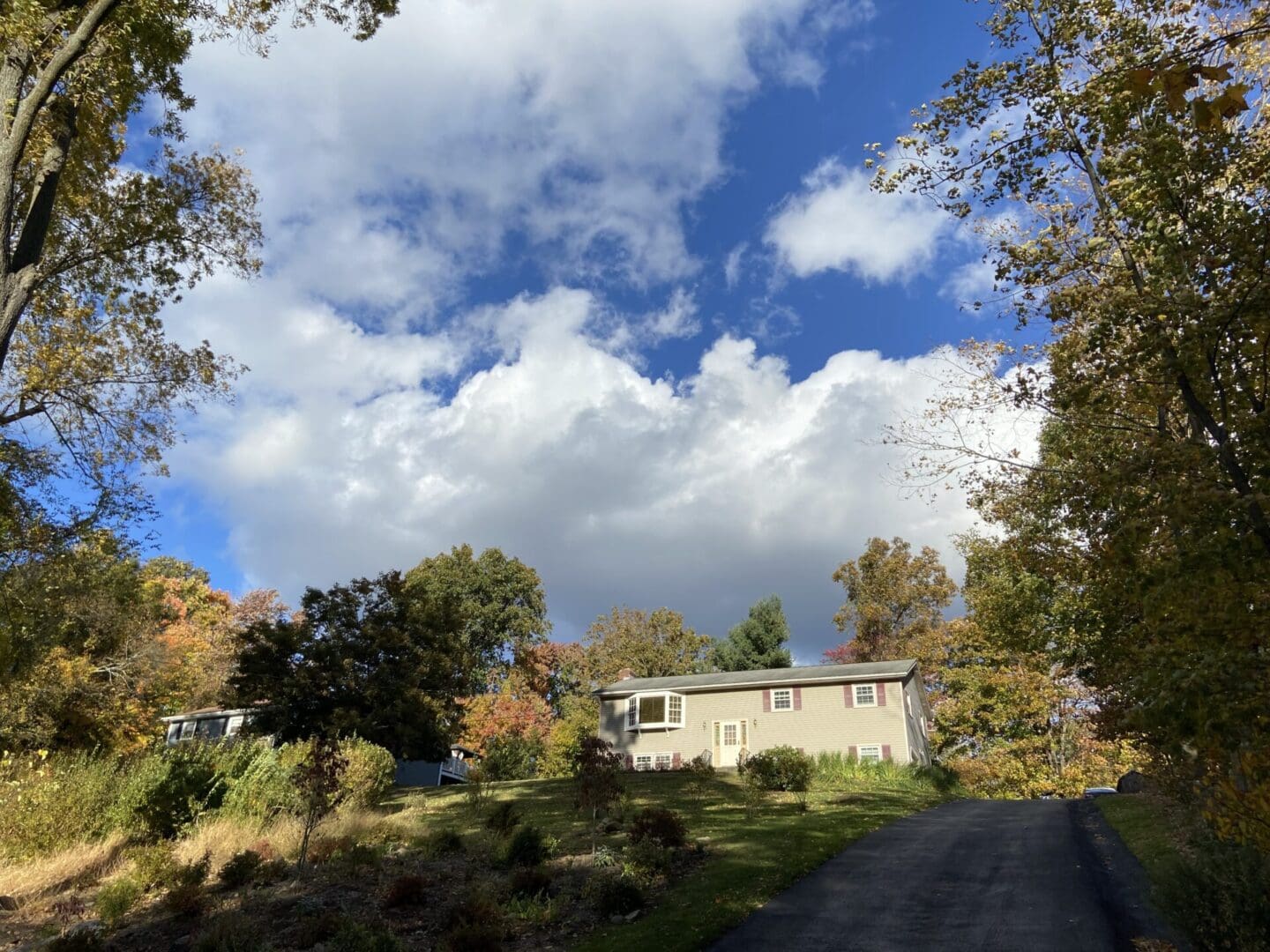 House with driveway, trees and sky.