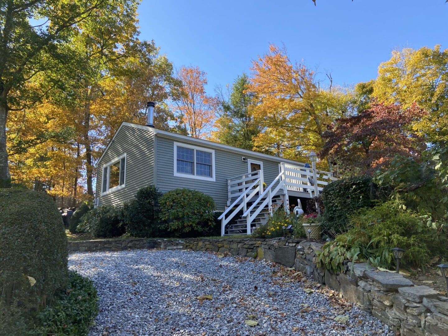 Gray house with fall foliage and a gravel driveway.